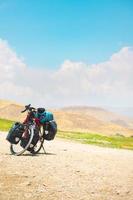 bicicletta in piedi su campagna ghiaia strada con no persona e montagne sfondo. completamente caricato viaggio in giro il mondo impostato su su Due ruote concetto foto