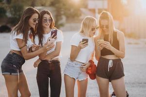 quattro attraente donne siamo in piedi su auto parcheggio con smartphone foto