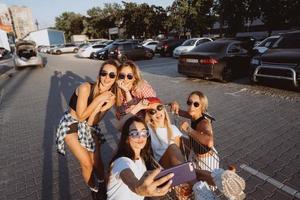cinque giovane ragazze avere divertimento con un' supermercato carrello su un' auto parco foto