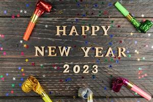 contento nuovo anno 2023 di legno lettere su di legno sfondo circondato festa multicolore fischia. festivo saluto carta per nuovo anno vacanze foto