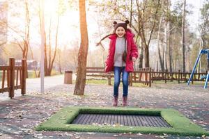 contento scuola ragazza salto su un' piccolo trampolino nel il parco foto