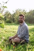 ritratto di giovane bello sorridente europeo uomo nel casuale capi di abbigliamento seduta su un' erba nel estate parco. foto