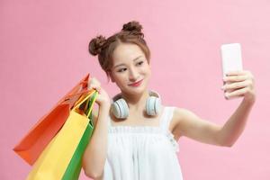 asiatico bellissimo contento giovane donna Tenere smartphone per autoscatto e shopping in linea con shopping borse su rosa sfondo. foto