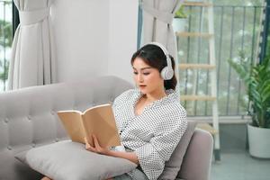ritratto bellissimo giovane asiatico donna leggere libro su divano nel vivente camera interno foto
