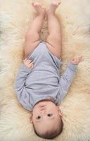 un' affascinante 7 mese vecchio bambino bugie nel letto nel un' grigio body foto