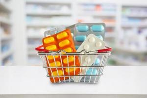 pacchetto di pillole medicinali nel carrello con gli scaffali della farmacia della farmacia sfocano lo sfondo foto