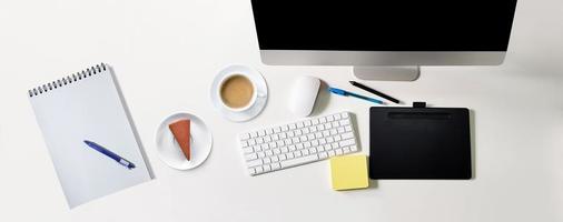 moderno bianca tavolo con nero schermo computer, caffè tazza, cioccolato torta. taccuino per scrittura messaggi, penna, superiore Visualizza, scrivania concetto foto