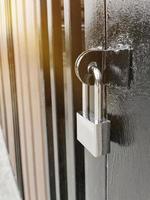 argento lucchetto chiuso e bloccato appendere su buco acciaio recinto cancello porta di casa con arancia leggero sera avvicinamento. foto
