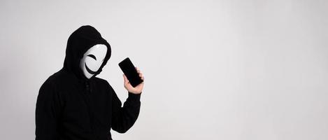 hacker anonimo e maschera facciale con smartphone in mano. foto