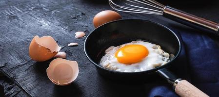 menù cucinando nel cucina uovo fritte uovo nel il padella e fresco crudo uova su nero di legno sfondo foto