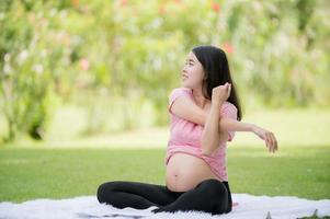 un' incinta asiatico donna rilassa con yoga allungamento esercizi nel il parco per il Salute di il madre e il nascituro bambino foto