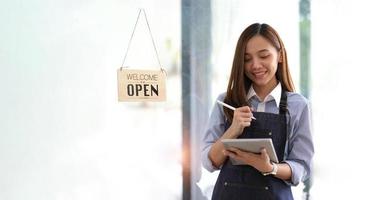 avvio di successo della piccola impresa titolare sme bellezza ragazza stand con tablet smartphone nel ristorante caffetteria. ritratto di donna asiatica abbronzata barista barista proprietario. concetto di business venditore imprenditore PMI foto