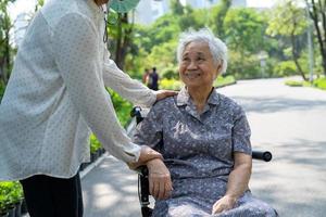 assistenza e cura del caregiver paziente asiatico anziano o anziano della donna che si siede sulla sedia a rotelle nel parco, concetto medico forte sano. foto