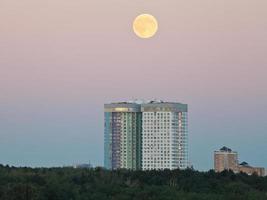 pieno Luna nel sera cielo al di sopra di urbano case foto