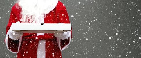 bianca Pizza scatola nel mani di Santa Claus nel bianca guanti, con un' barba, nel un' rosso cappotto. Natale veloce cibo consegna. nuovo anni vigilia promozione. ristorazione. copia spazio, finto su. bandiera foto