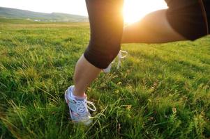 gambe dell'atleta del corridore che corrono sul campo di erba soleggiato