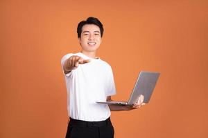 asiatico uomo Tenere computer portatile, isolato su arancia sfondo foto