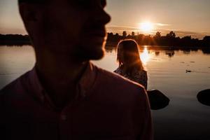 silhouette di coppia nel amore vicino il lago su tramonto. bello contento coppia avendo divertimento vicino all'aperto. contento vacanza concetto. selettivo messa a fuoco foto