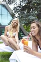 Due giovane donna rilassante su lettini. attraente giovane femmina amici avendo divertimento vicino nuoto piscina. foto