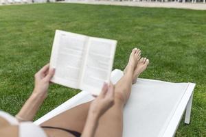 giovane donna lettura un' libro di il bordo piscina. foto
