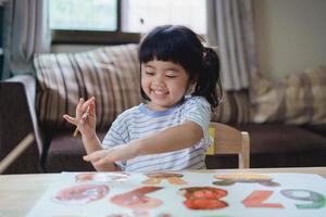 carino poco asiatico bambino sorridente pittura con colorato vernici utilizzando acquerello. asiatico ragazza utilizzando pennello disegno colore. bambino attività stile di vita concetto. foto