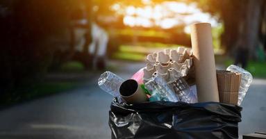 proprietario di casa è separare bottiglie, carta, uovo cartoni e altro cose nel il nero plastica Borsa nel davanti di il Casa, concetto per riducendo globale riscaldamento, Salvataggio nostro mondo, morbido e selettivo messa a fuoco. foto