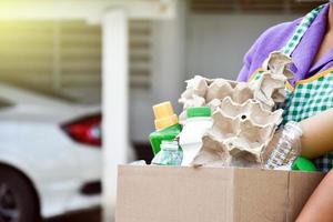 proprietario di casa è separare bottiglie, carta, uovo cartoni e altro cose nel il nero plastica Borsa nel davanti di il Casa, concetto per riducendo globale riscaldamento, Salvataggio nostro mondo, morbido e selettivo messa a fuoco. foto