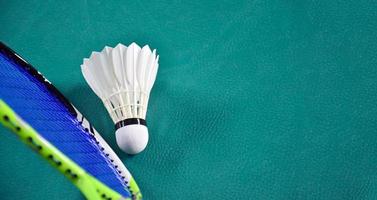 volano e racchetta da badminton bianco crema con ombreggiatura di luce al neon sul pavimento verde in un campo da badminton al coperto, sfondo sfocato di badminton, spazio per la copia. foto