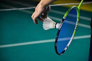 badminton giocatore detiene racchetta e bianca crema volano nel davanti di il netto prima servendo esso per un altro lato di il Tribunale. foto