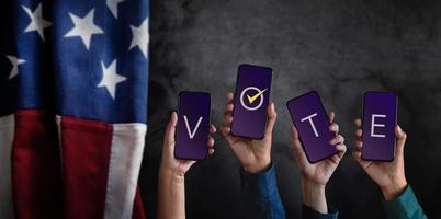 voto concetto. elezione nel America. gruppo di persone sollevato mobile Telefono con testo votazione. sfocato bandiera di unito stati come sfondo foto