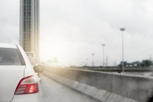 astratto posteriore lato di bianca auto su il concreare strada con piovoso ambiente. calcestruzzo parete su il lato di il strada. grattacielo Residenziale edificio nel davanti. foto