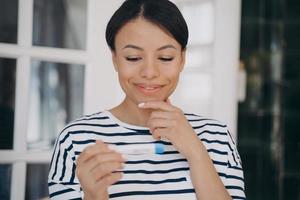 bello giovane donna guardare a gravidanza test e sorridente. Soddisfatto signora Tenere ovulazione test. foto