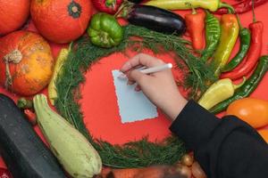 verdure siamo di cui su in giro un' foglio di carta e un' matita. vuoto spazio per testo. femmina mano scrittura un' ricetta su un' vuoto vuoto su un' rosso sfondo. foto