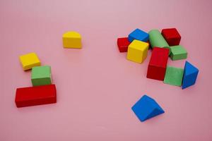 colorato di legno blocchi su rosa sfondo. creatività giocattoli. figli di edificio blocchi. geometrico forme - cubo, triangolare prisma, cilindro. il concetto di logico pensiero. foto