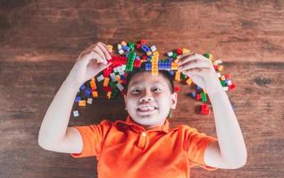 asiatico bambini menzogna giù su di legno piani giocare con colorato plastica giocattolo blocchi, e avere divertimento edificio e la creazione di a casa.