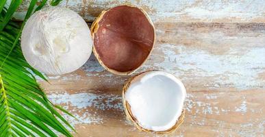 un' fresco Noce di cocco con bucce tagliare nel metà rivelatrice bianca Noce di cocco carne e Noce di cocco le foglie su un vecchio di legno sfondo. foto