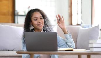 felicissimo del Millennio femmina alunno nel cuffie Guarda a il computer portatile schermo studia in linea a partire dal casa. contento giovane misto gara donna nel auricolari parlare su video chiamata con insegnante. virtuale evento concetto. foto