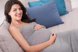 incinta donna seduta su divano a casa foto