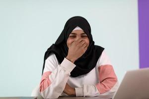 afro musulmano donna indossare un' hijab si siede sorridente nel sua casa ufficio e usi un' il computer portatile foto