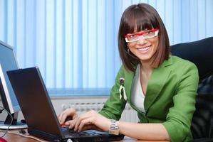 sorridente giovane donna d'affari Lavorando su un' il computer portatile nel il ufficio. foto