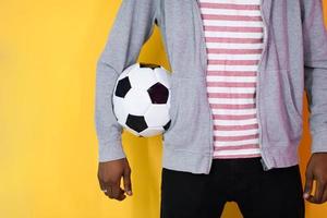 afro uomo in posa su un' giallo sfondo mentre Tenere un' calcio palla foto