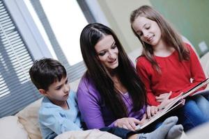 giovane mamma giocare con loro bambini a casa e lettura libro foto