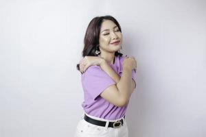 giovane bellissimo asiatico donna indossare un' lilla viola maglietta al di sopra di bianca sfondo abbracciare se stessa contento e positivo, sorridente fiducioso. amore per se stessi e automedicazione foto
