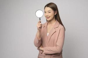 giovane asiatico donna Tenere ingrandimento bicchiere al di sopra di bianca sfondo, analisi e finanza concetto. foto
