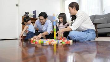 asiatico famiglia con bambini giocando e edificio Torre di colorato di legno giocattolo blocchi nel vivente camera a casa, educativo gioco. foto