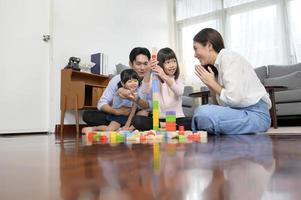 asiatico famiglia con bambini giocando e edificio Torre di colorato di legno giocattolo blocchi nel vivente camera a casa, educativo gioco. foto