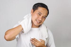 ritratto di attraente uomo asiatico che si pulisce il viso con un asciugamano dopo il peeling, maschera, inumidimento, effettuando ogni procedura mattutina, guardando la fotocamera foto