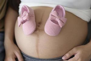 giovane donna incinta che mette le scarpe per bambini sul concetto di cura della pancia, della famiglia e della gravidanza foto