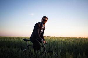 un uomo d'affari caucasico in sella a una bicicletta nei campi estivi, maschio in giacca e cravatta su una bici fissa. foto