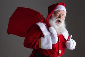 Babbo Natale con gli occhiali sta guardando la fotocamera e sorridente, su sfondo grigio foto